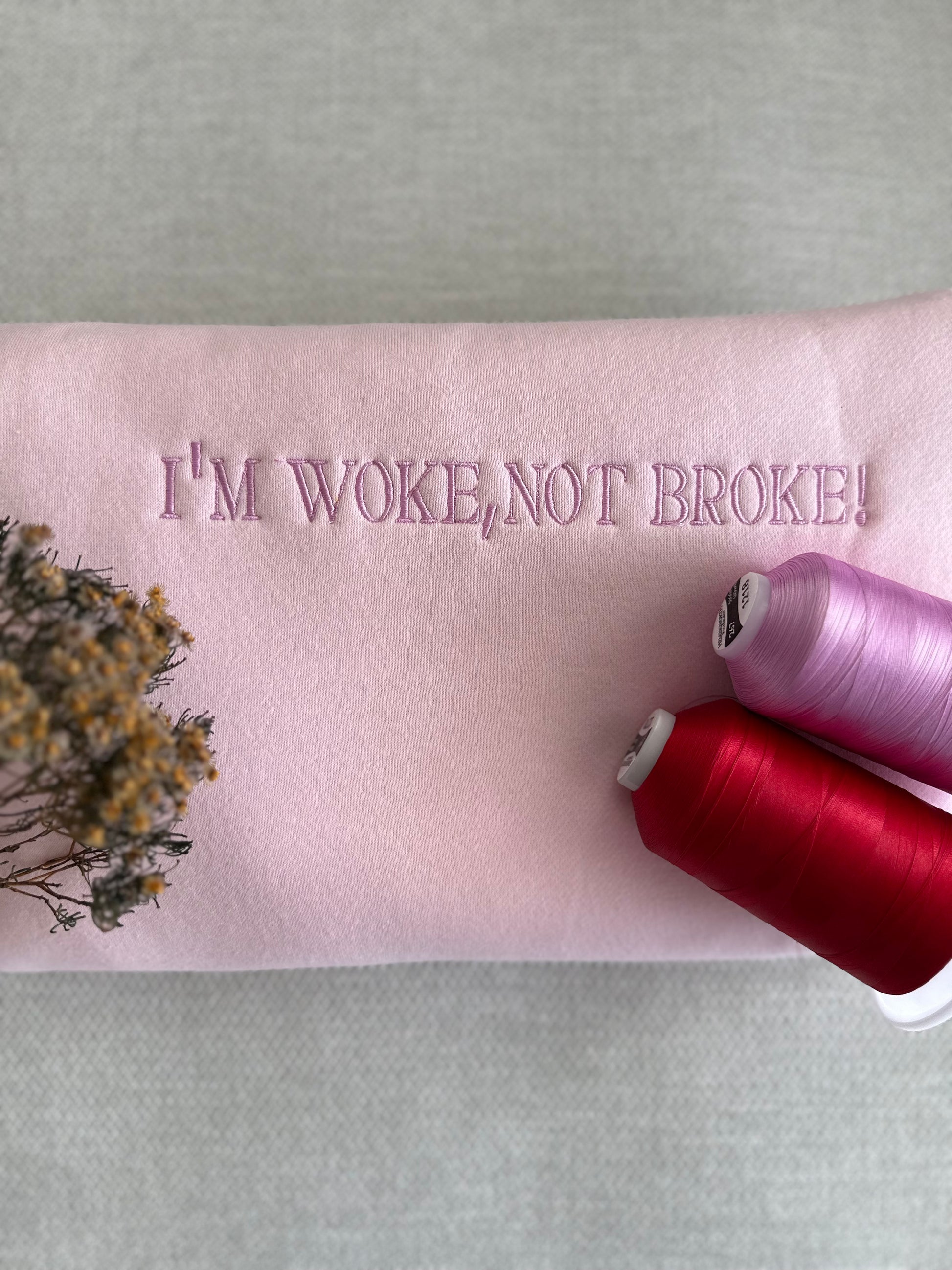 Pink fabric with 'I'M WOKE, NOT BROKE!' text and spools of thread on a light gray background