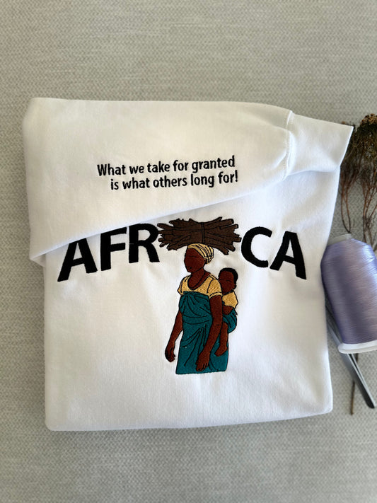 Folded white shirt with 'AFRICA' text and graphic of a woman and child on a gray surface.