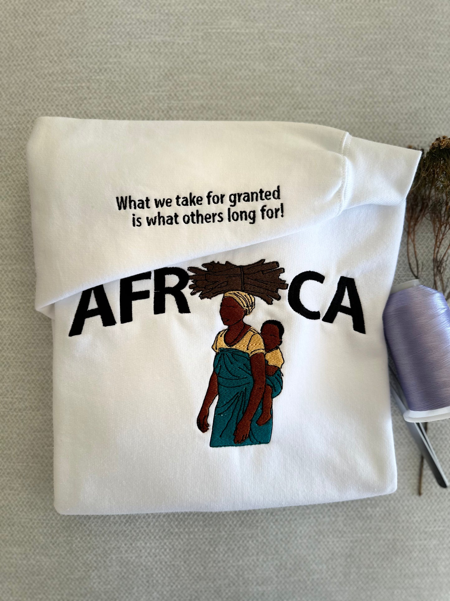 Folded white shirt with 'AFRICA' text and graphic of a woman and child on a gray surface.