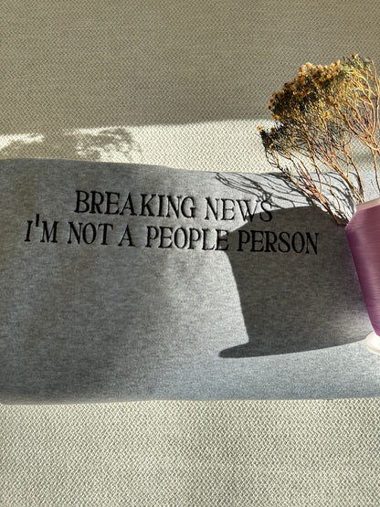Text 'BREAKING NEWS I'M NOT A PEOPLE PERSON' on a gray surface with a plant in the background. Brisbane embroidery