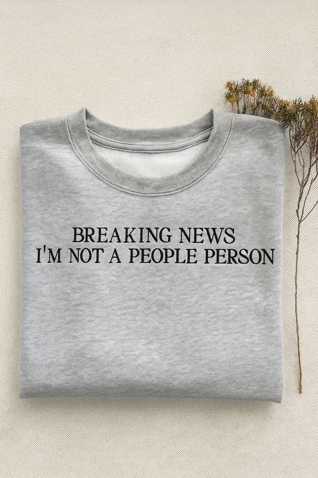 Gray sweatshirt with 'BREAKING NEWS I'M NOT A PEOPLE PERSON' text on a beige background. Brisbane embroidery