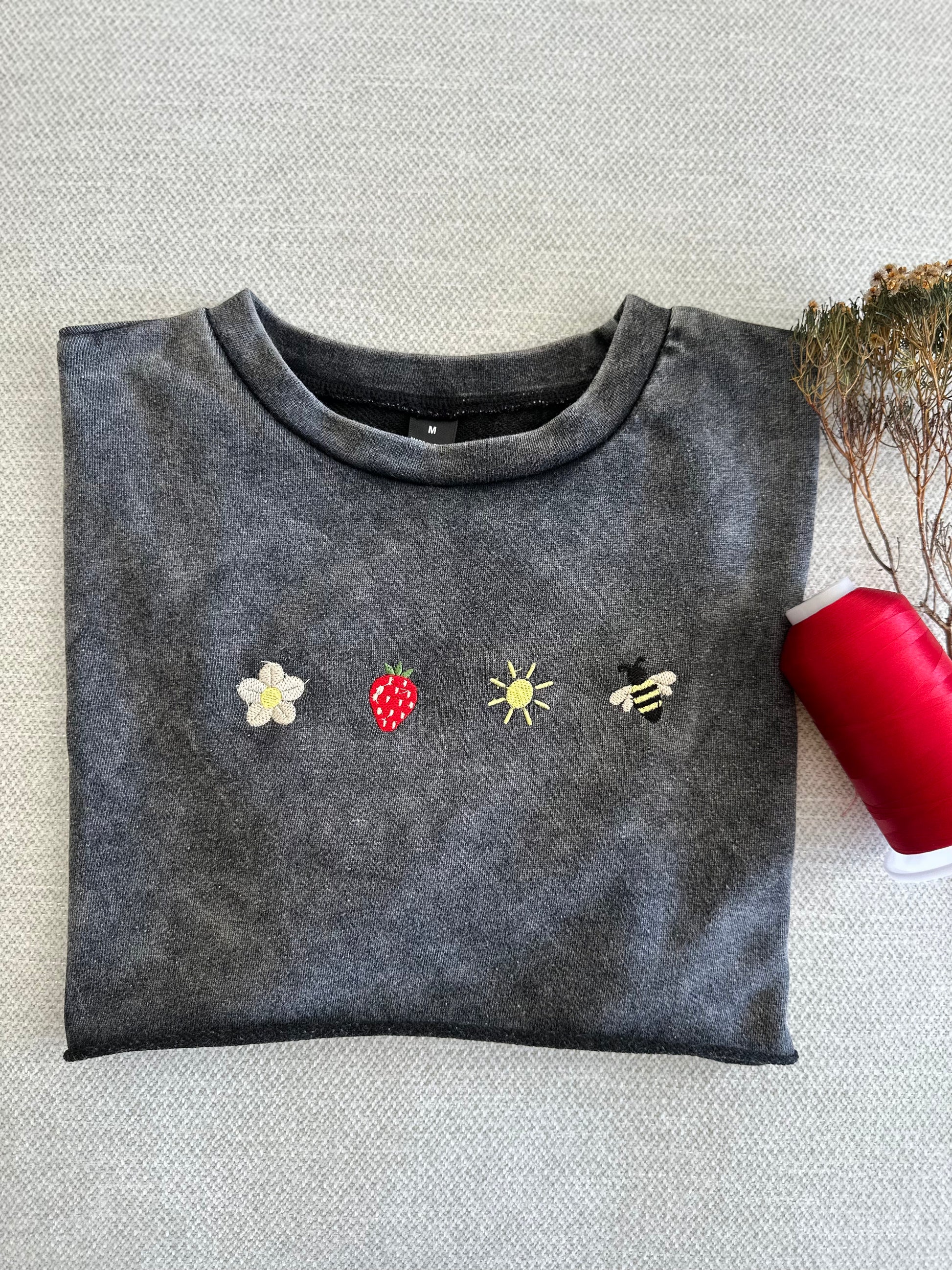 Folded dark gray sweatshirt with embroidered designs on a textured surface