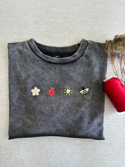 Folded dark gray sweatshirt with embroidered designs on a textured surface